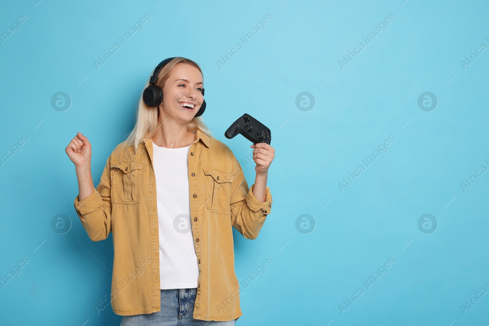 Photo of Woman in headphones with controller on light blue background, space for text