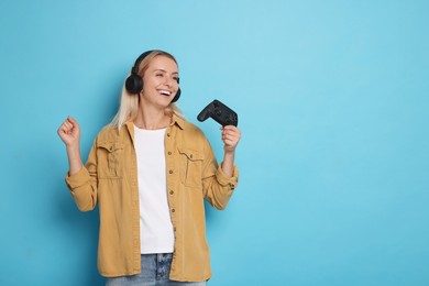 Woman in headphones with controller on light blue background, space for text