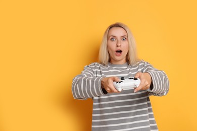 Photo of Emotional woman playing video games with controller on orange background, space for text