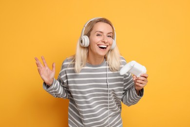 Photo of Happy woman in headphones with controller on orange background