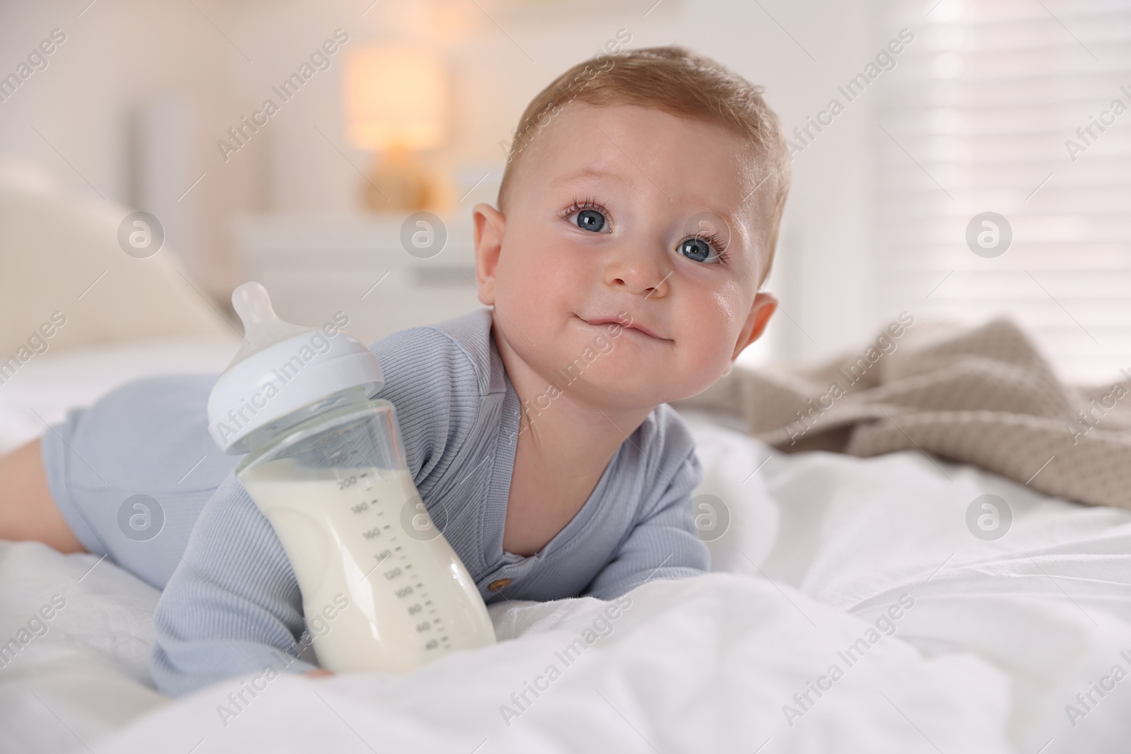 Photo of Cute little baby with bottle of milk on bed indoors