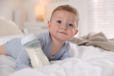 Cute little baby with bottle of milk on bed indoors