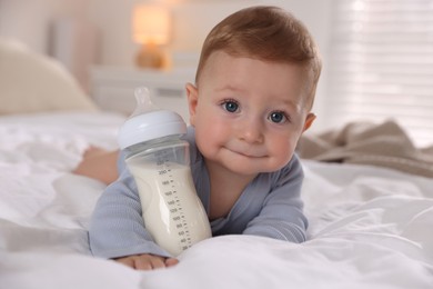 Cute little baby with bottle of milk on bed indoors