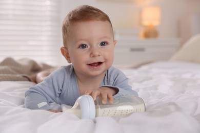 Cute little baby with bottle of milk on bed indoors