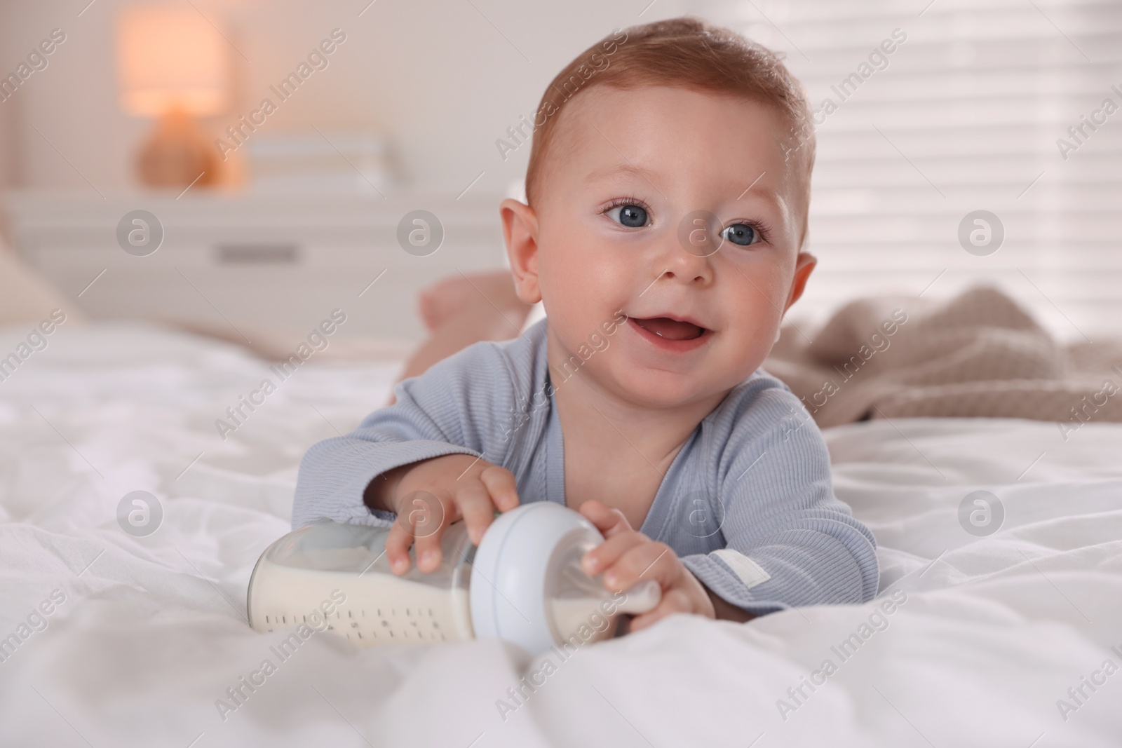 Photo of Cute little baby with bottle of milk on bed indoors