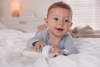 Cute little baby with bottle of milk on bed indoors