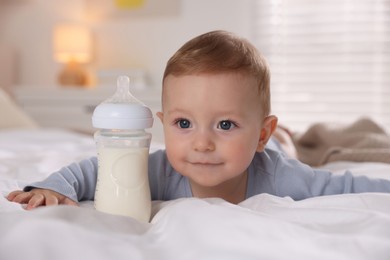 Photo of Cute little baby with bottle of milk on bed indoors