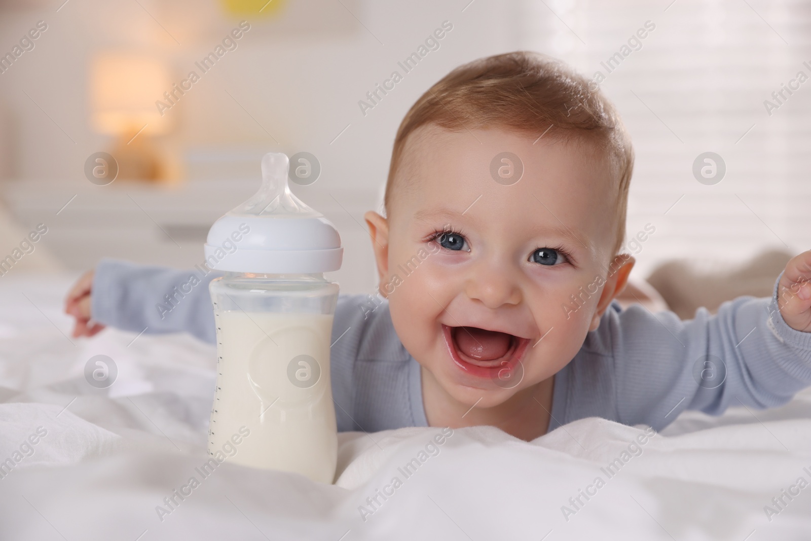 Photo of Cute little baby with bottle of milk on bed indoors