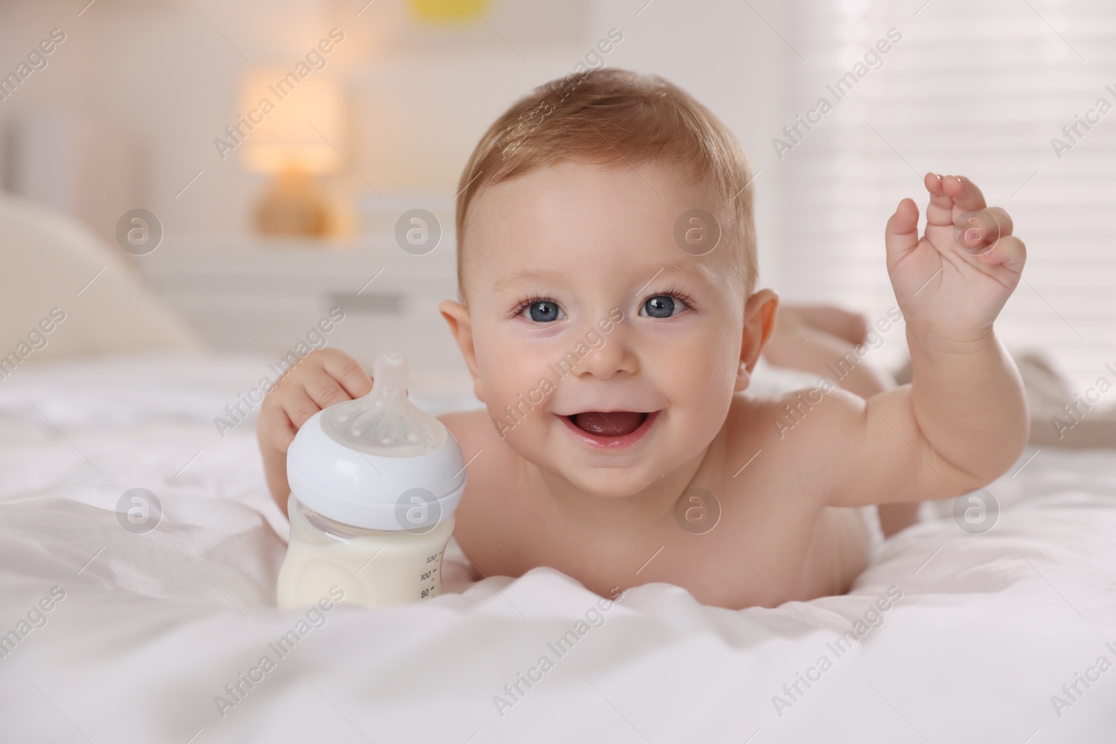 Photo of Cute little baby with bottle of milk on bed indoors