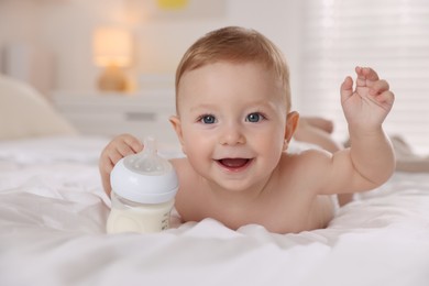 Cute little baby with bottle of milk on bed indoors