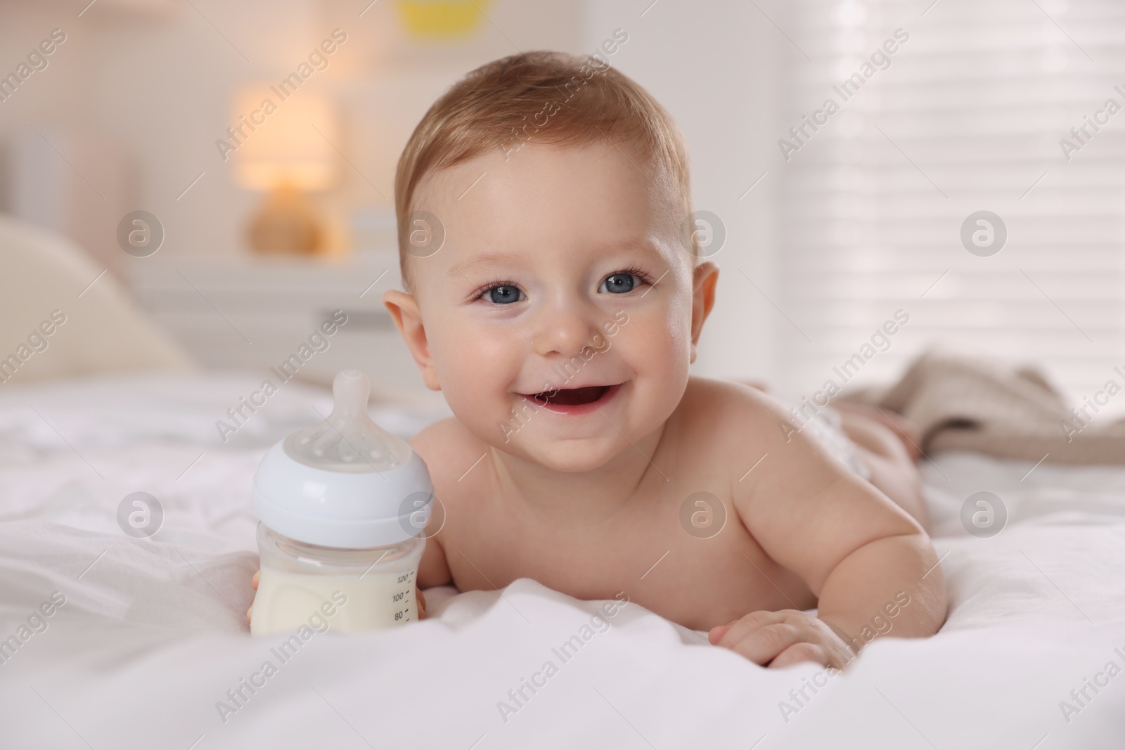 Photo of Cute little baby with bottle of milk on bed indoors