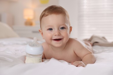 Cute little baby with bottle of milk on bed indoors