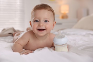 Cute little baby with bottle of milk on bed indoors