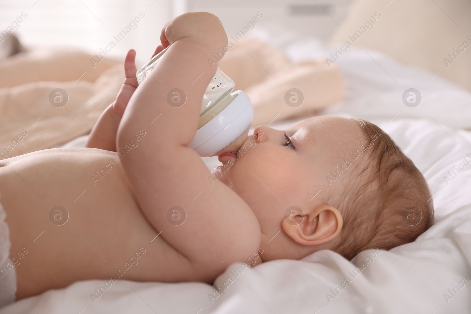 Photo of Cute little baby with bottle of milk on bed