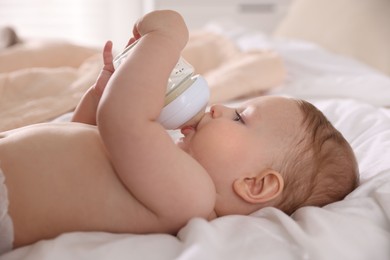 Cute little baby with bottle of milk on bed