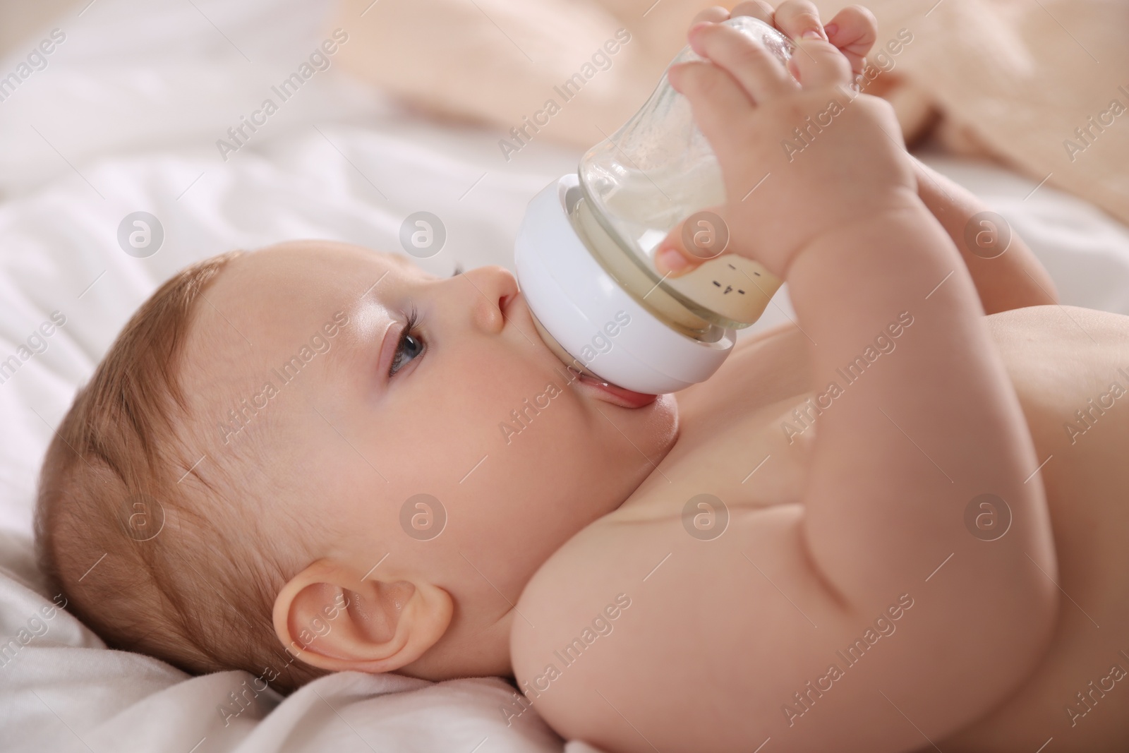 Photo of Cute little baby with bottle of milk on bed