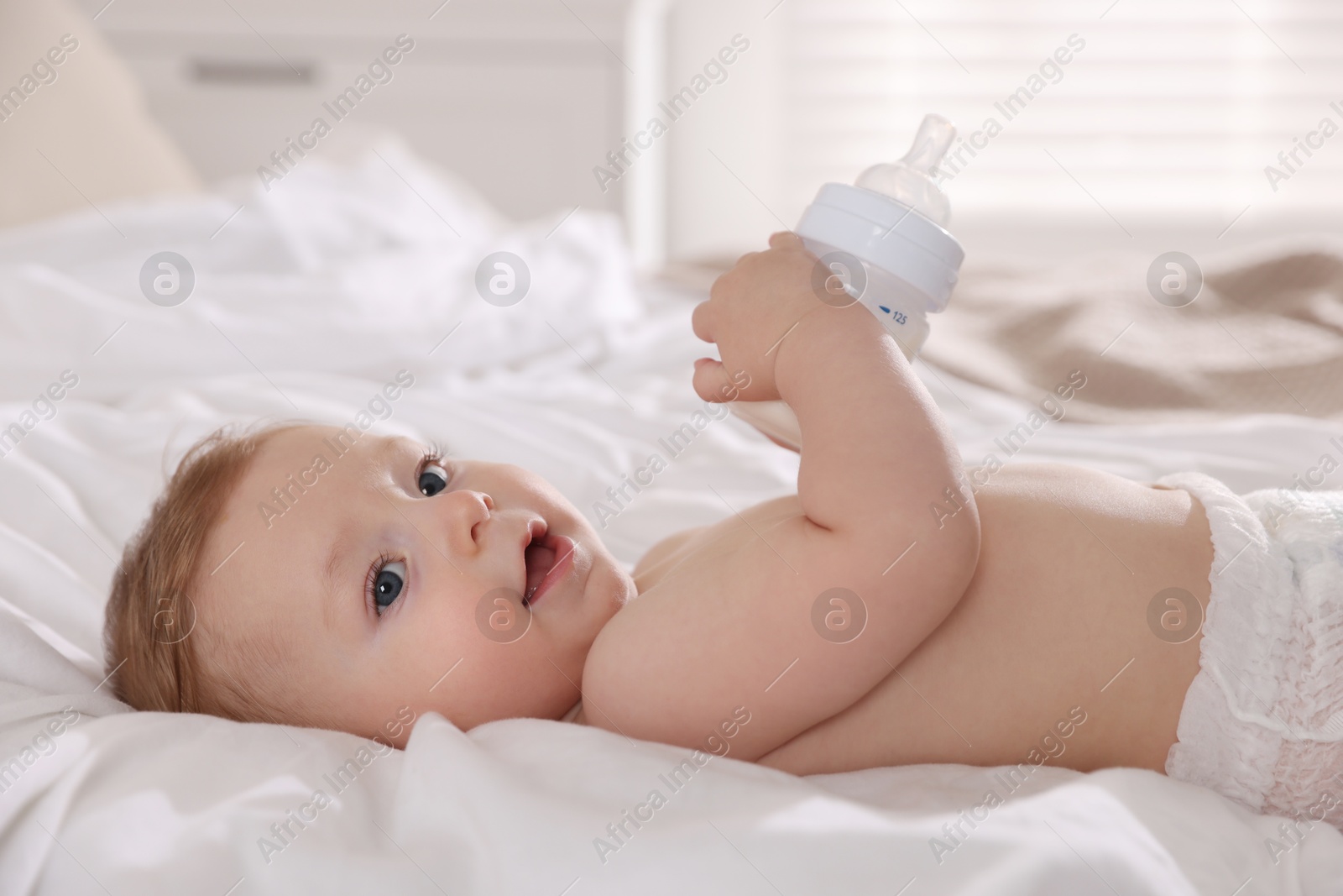 Photo of Cute little baby with bottle of milk on bed indoors