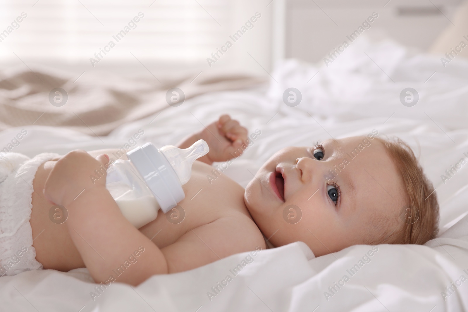 Photo of Cute little baby with bottle of milk on bed indoors