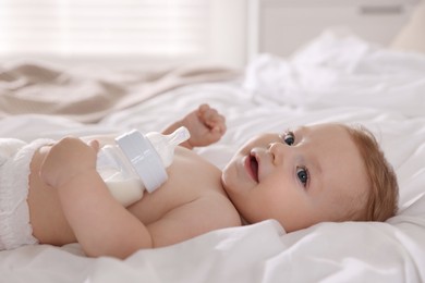 Cute little baby with bottle of milk on bed indoors