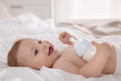 Cute little baby with bottle of milk on bed indoors