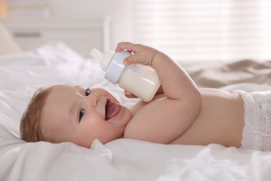 Cute little baby with bottle of milk on bed indoors