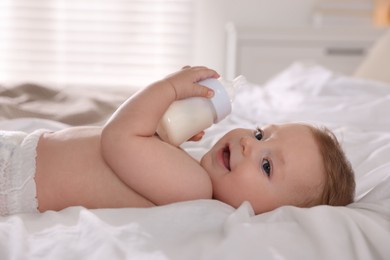 Cute little baby with bottle of milk on bed indoors