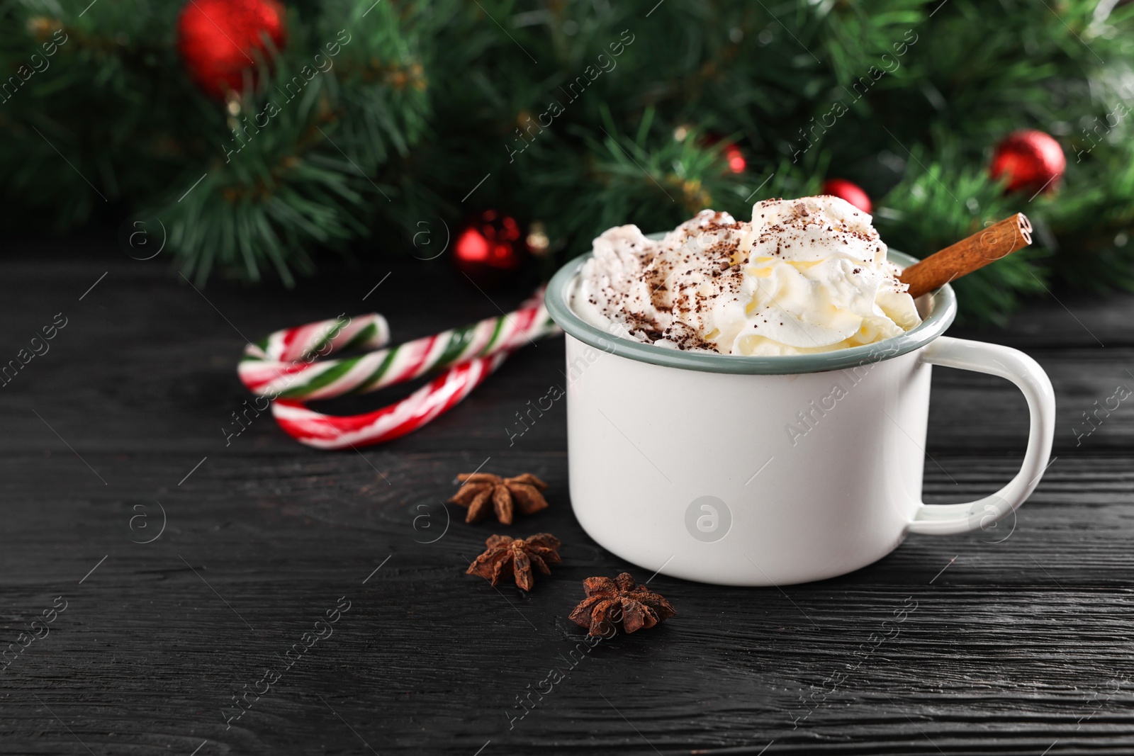 Photo of Tasty hot cocoa drink with whipped cream in mug and spices on black wooden table, space for text