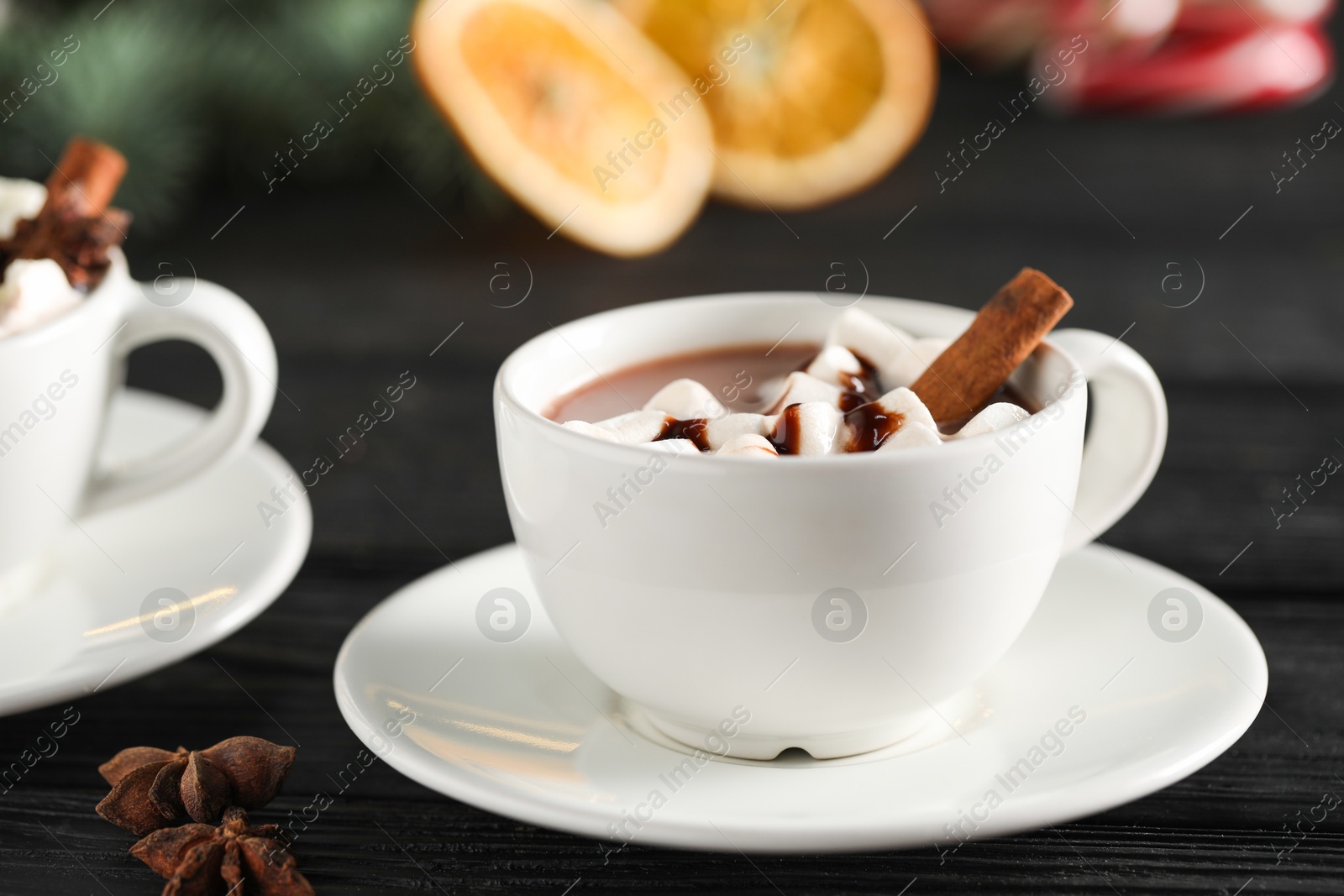 Photo of Tasty hot cocoa drink with marshmallows in cups and spices on black wooden table, closeup