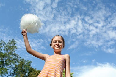 Photo of Little girl with sweet cotton candy against blue sky in park, low angle view