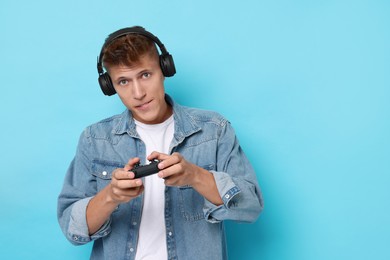 Photo of Young man in headphones playing video games with controller on light blue background, space for text