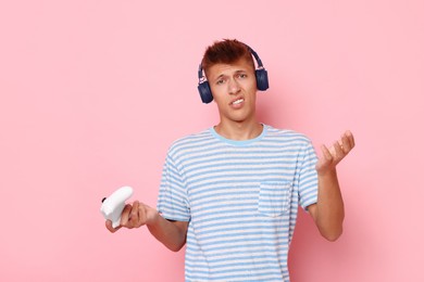 Photo of Unhappy young man in headphones with controller on pink background