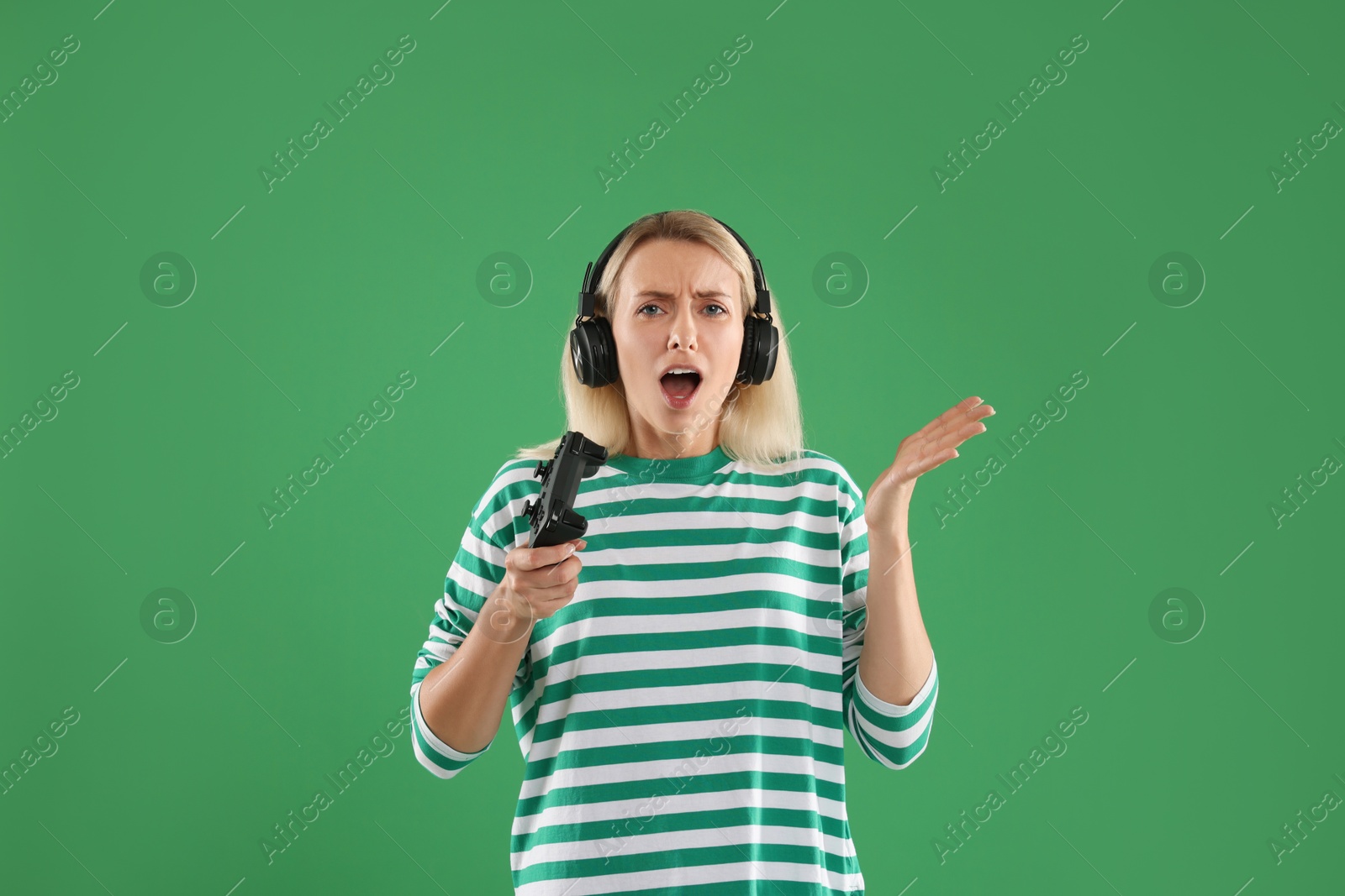 Photo of Emotional woman in headphones with controller on green background