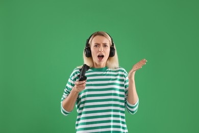 Photo of Emotional woman in headphones with controller on green background