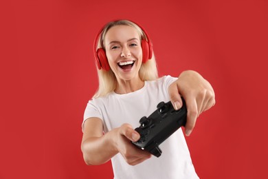 Photo of Happy woman in headphones playing video games with controller on red background