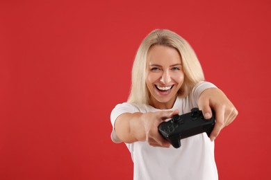 Photo of Happy woman playing video games with controller on red background, space for text