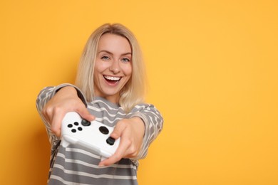 Happy woman playing video games with controller on orange background, space for text