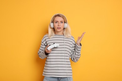 Surprised woman in headphones with controller on orange background