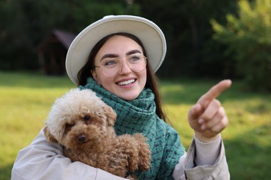 Smiling woman pointing at something to cute dog in autumn park