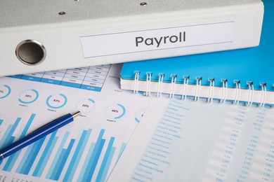 Photo of Payroll. Pen, notebook and graphical charts on table