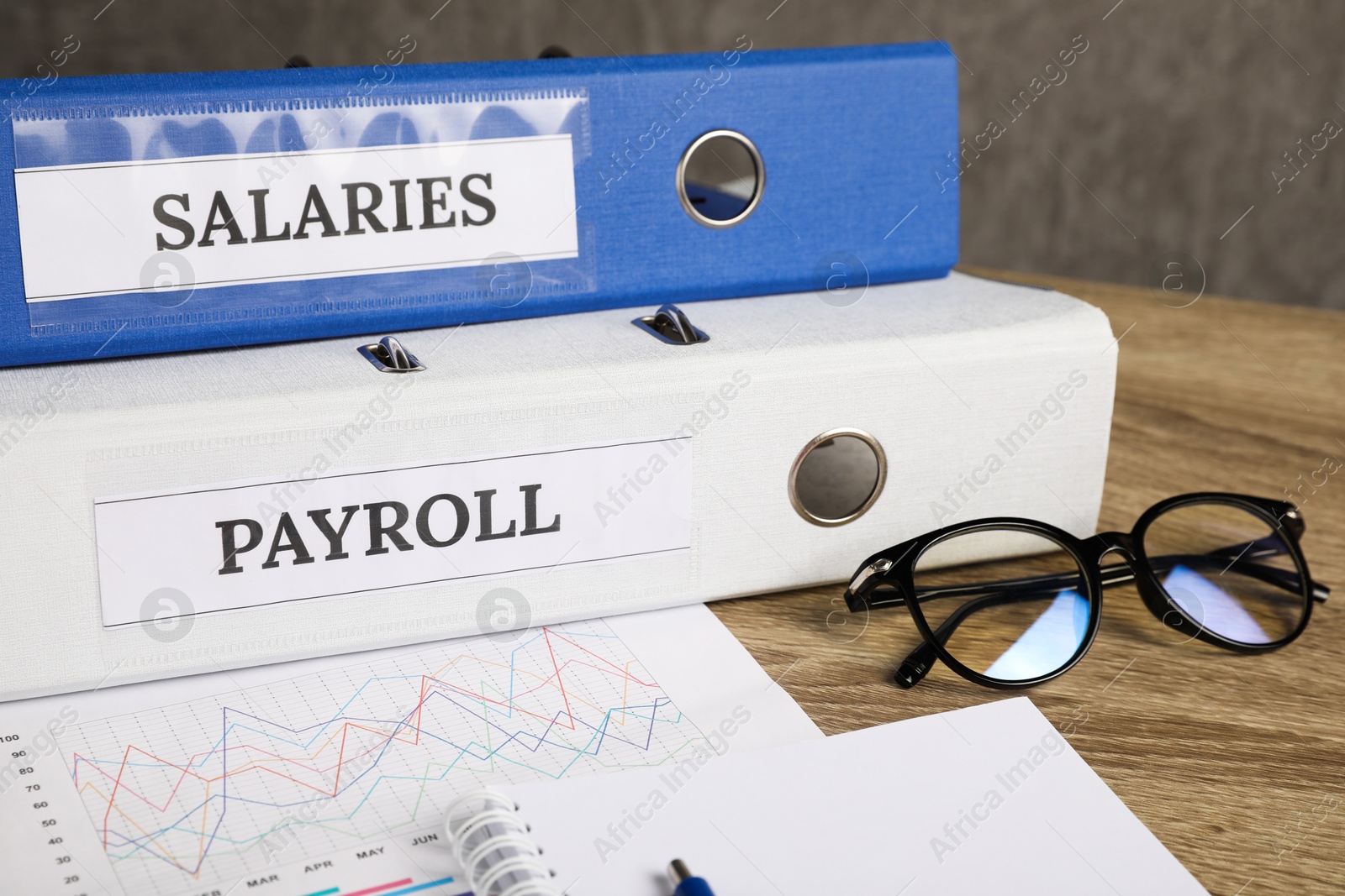 Photo of Payroll. Glasses, notebook and graphical chart on wooden table