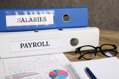 Photo of Payroll. Glasses, notebook, graphical charts and pen on wooden table