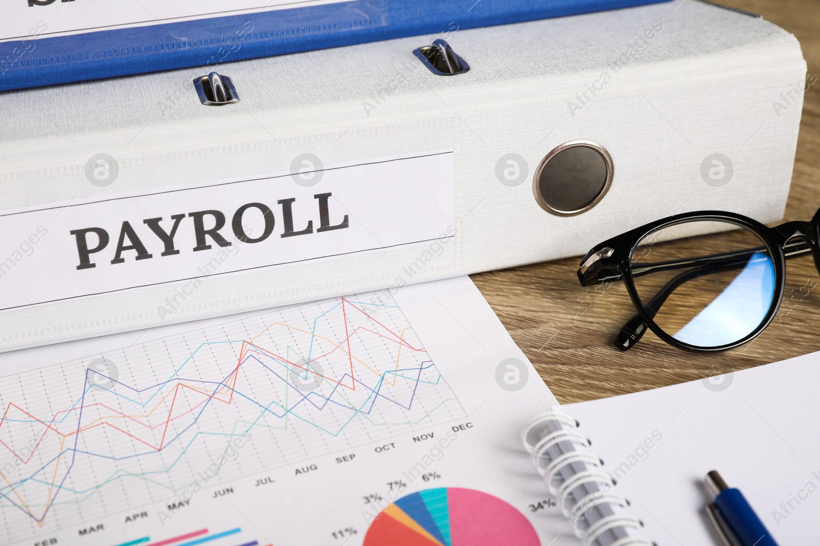 Photo of Payroll. Glasses, notebook, graphical charts and pen on wooden table