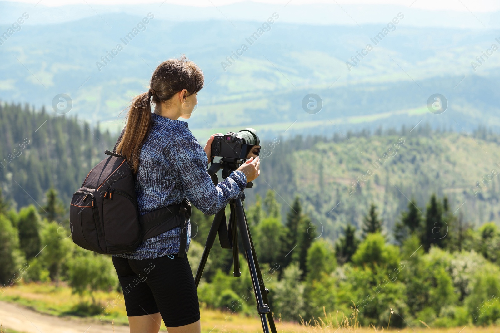 Photo of Photographer with backpack and camera on tripod taking picture of beautiful mountains. Space for text