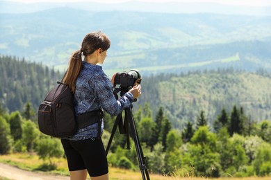 Photographer with backpack and camera on tripod taking picture of beautiful mountains. Space for text