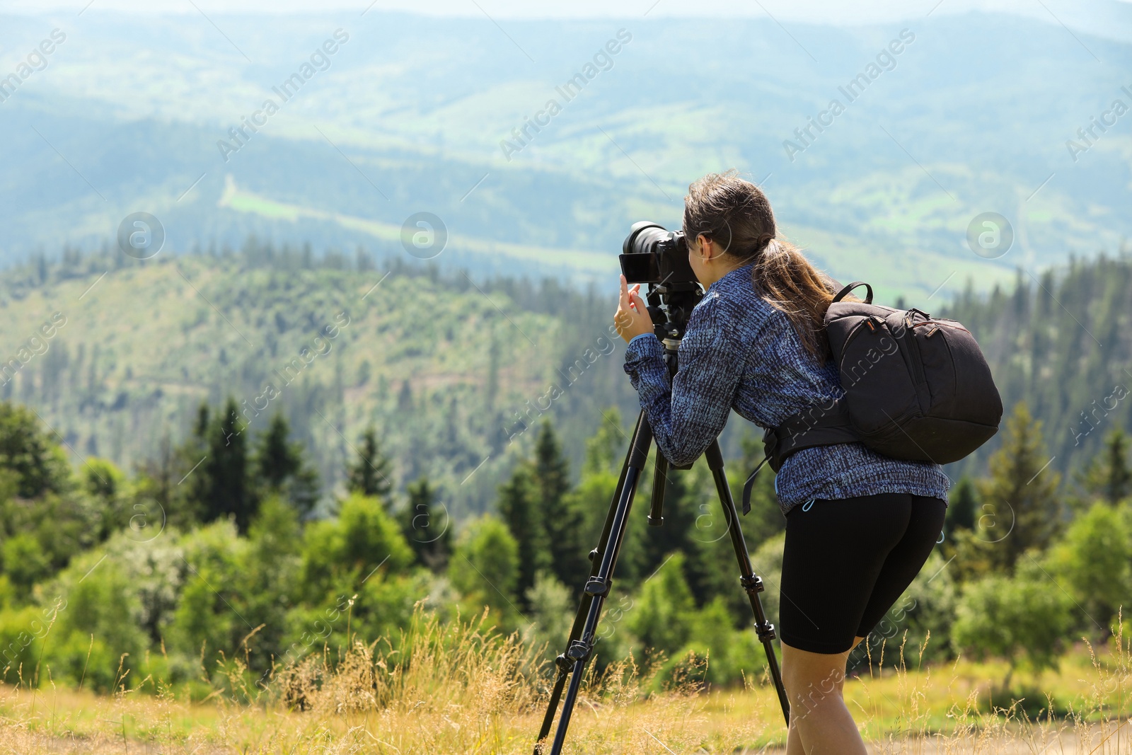 Photo of Photographer with backpack and camera on tripod taking picture of beautiful mountains. Space for text