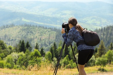 Photographer with backpack and camera on tripod taking picture of beautiful mountains. Space for text