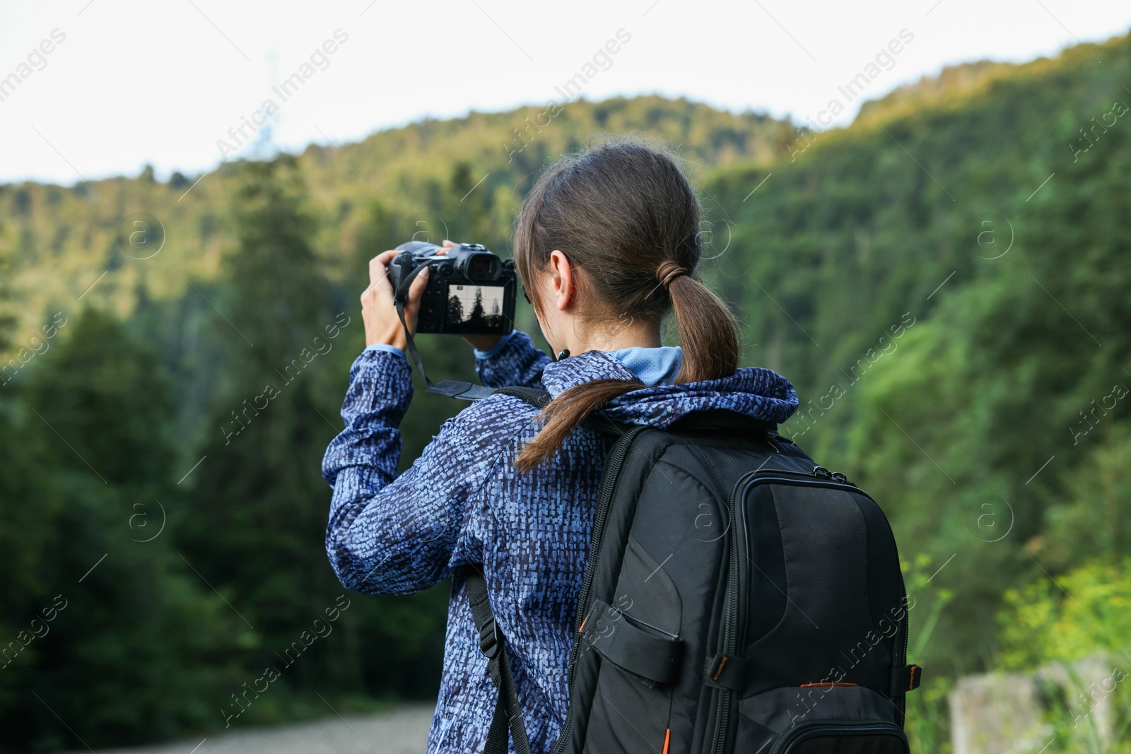 Photo of Photographer with backpack and camera taking picture of beautiful mountains, back view