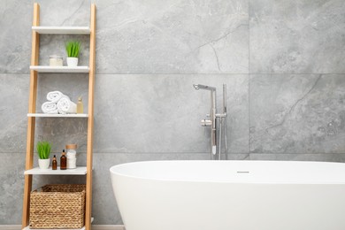 Photo of Bath tub and shelf near light grey wall in bathroom