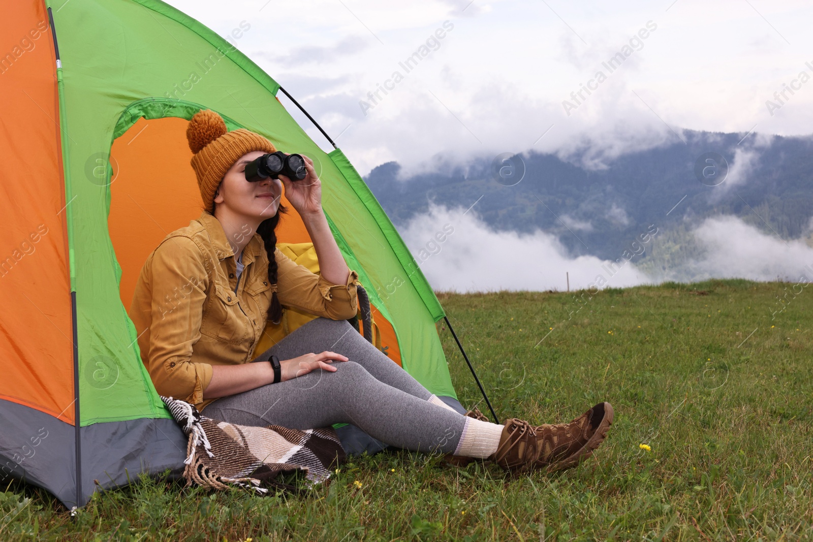 Photo of Young camper with binoculars and tent in mountains, space for text. Active tourism