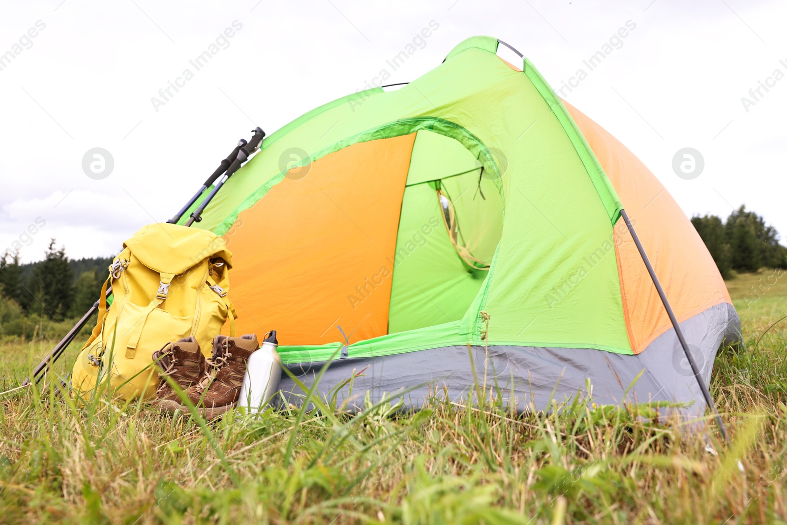 Photo of Tent, backpack, trekking poles and thermos on green grass in mountains